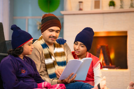 Indian middle aged father telling stories to sibling kid from book during night at home during winter holidays - concept of family bonding, togetherness and fatherhoodの写真素材