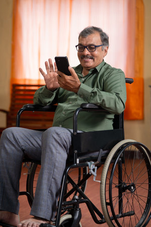 Vertical shot of happy elderly senior man with disability on wheelchair using mobile phone at home - concept of technology, social media and digital technologyの写真素材