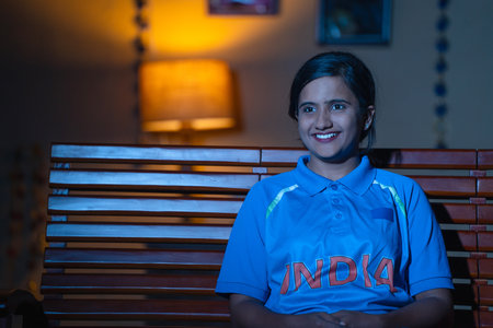 Curios young girl in indian jersey watching Cricket match on tv or television at home - concept of Supporter, and championship.の写真素材