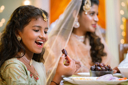 Happy excited indian girl eating dates while having dinner during Ramadan iftar or dinner with family - concept of healthy eating, ramzan iftar and relationshipの写真素材