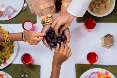 Top view shot of indian husband with kids taking dates from Muslim women during ramadan feast at home - concept of Ramadan feast, iftar and bondingの写真素材