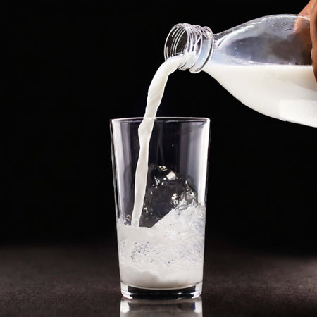 Pouring milk into a glass on a black background. Close upの素材
