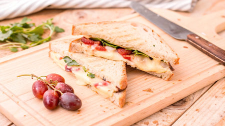 sandwich with ham, cheese, grapes and arugula on wooden boardの写真素材