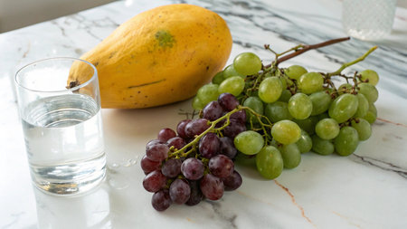 Grapes and a glass of water on a white marble table