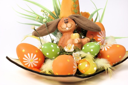 Easter decoration - bunny in a wicker basket with flowers and eggs in green, orange and yellowの写真素材