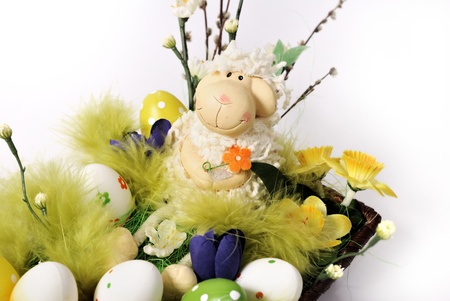 Easter decoration - lamb in a wicker basket with flowers and eggs in green, white and yellowの写真素材