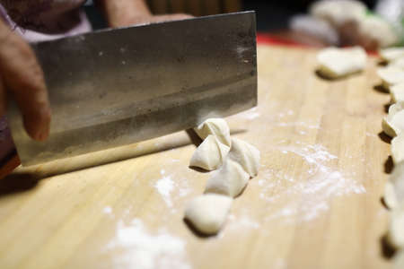 Chef preparing dumplings on a wooden board with a knifeの写真素材