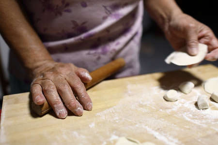 An elderly woman rolls out the dough with a rolling pin. Selective focus.の写真素材