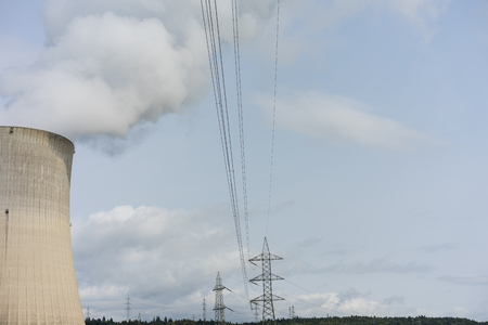 nuclear power plant chimney with condensation smoke on a cloudy day with power pole electricity tower in the backの写真素材