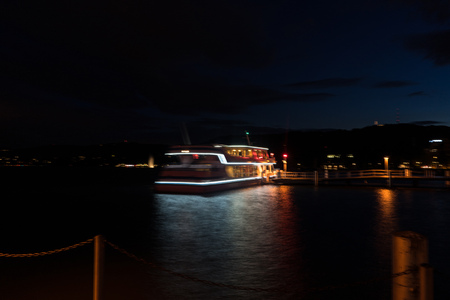 cruise ship with lights on at night on lake zurich with water reflectionsの写真素材