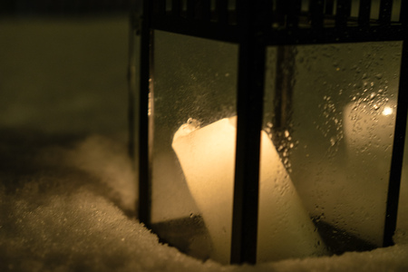 Candle burning in lantern standing in snow at nightの写真素材