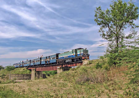 Old, 2 feet 6 inches , narrow gauge `Shakuntala` railway with few roof-top commuters crosses an old...