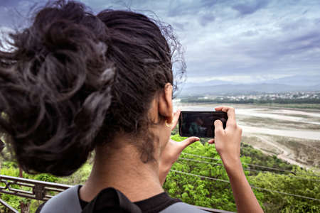 Jammu, India - April 18th, 2019 : Young lady capturing a nature scene with her cell phone.の写真素材