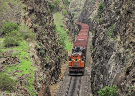 Diesel locomotive hauling a goods train through a deep rock cutting in Shindawane, Maharashtra,...
