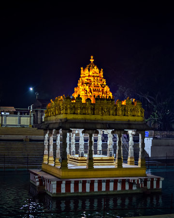 Night image of illuminated temple with golden dome reflected in water pond at Tirupati, Andra Pradesh, Indiaの写真素材