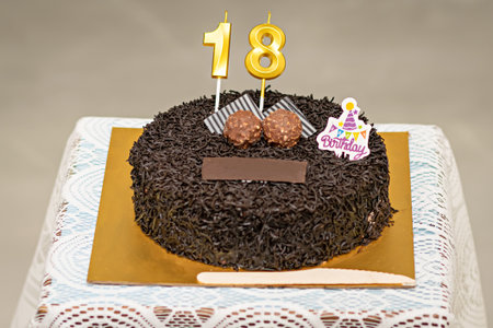 Close up image of a brown textured cake with golden letters of 18 and some decorations , ready for...