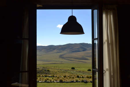 Sunny mountain valley view framed by wooden window and ceiling lamp. Looking outside from window.の写真素材