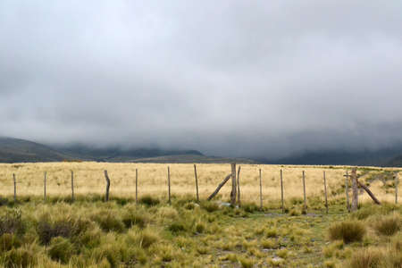 Low dark grey clouds over mountain field with rustic wood and wire fence.の写真素材