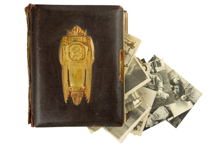 Vintage photo album (circa 1900) with buckle, brass engraved decoration and falling out retro photos (circa 50s) isolated on whiteの写真素材
