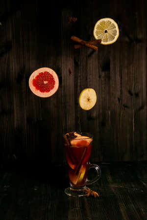 christmas mulled wine, in a transparent glass with fruit on a dark wooden background surrounded by flying spices and fruitsの写真素材