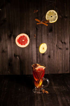 christmas mulled wine, in a transparent glass with fruit on a dark wooden background surrounded by flying spices and fruitsの写真素材
