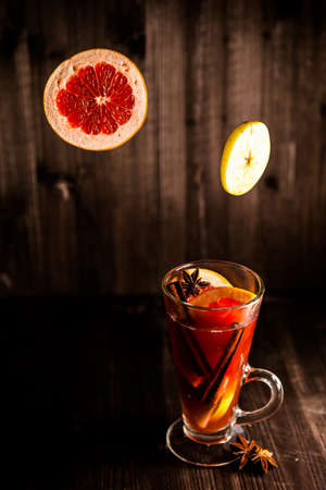 christmas mulled wine, in a transparent glass with fruit on a dark wooden background surrounded by flying spices and fruitsの写真素材