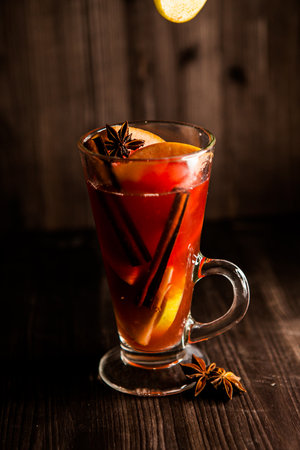 christmas mulled wine, in a transparent glass with fruit on a dark wooden background surrounded by flying spices and fruitsの写真素材
