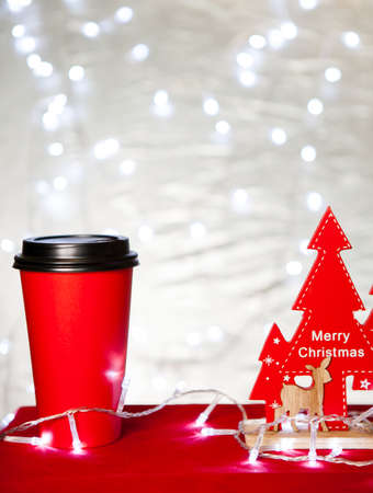 red Paper cup of coffee surrounded by Christmas decorations on Christmas lights bokeh backgroundの写真素材