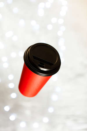 red paper cup for coffee flying in the air against the background of New Year's lighting bokeh