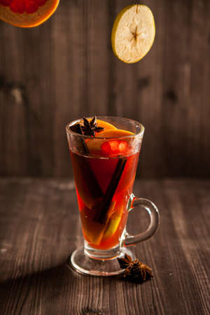 christmas mulled wine, in a transparent glass with fruit on a dark wooden background surrounded by flying spices and fruitsの写真素材