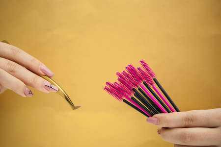 eyelash extension tools, golden tweezers and pink-black brushes on a gold backgroundの写真素材