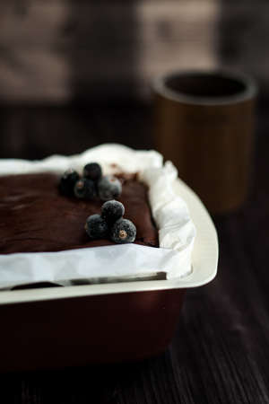 brownie cake garnished with frozen blackcurrant berries in a brown mold with white parchment on a dark backgroundの写真素材