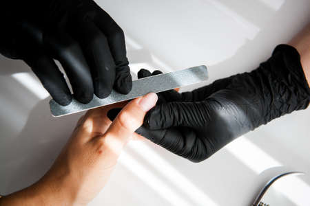 a master in black vinyl gloves gives a manicure to a white girl. shaping nails with a nail stick