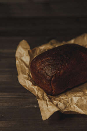 freshly baked black rye bread on a dark background and on craft paper. Dark moody background with...