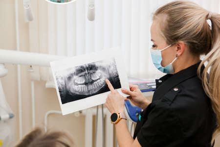 White woman blonde doctor dentist showing x-ray picture to patientの写真素材