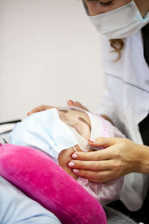 A girl makes the procedure for extending eyelashes during a pandemic, a master with tools in his handsの写真素材