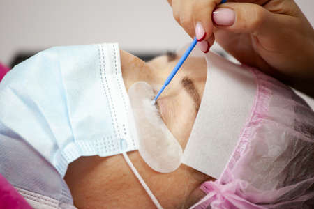 A girl makes the procedure for extending eyelashes during a pandemic, a master with tools in his...