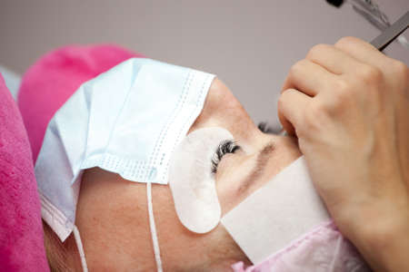 A girl makes the procedure for extending eyelashes during a pandemic, a master with tools in his...