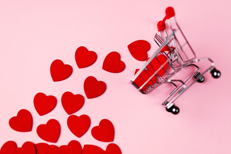 Flat lay view of hearts getting out from supermarket trolley basket on a pink background. Valentine's day conceptの写真素材