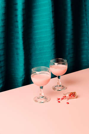 Two glass of wine with creative drink and pills look a like or sweer candy lay on a floor with small bottle against pink background and blue cyan silk fabric.の写真素材