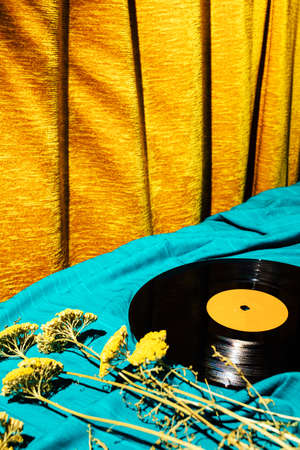 Retro styled image of LP vinyl record on a cyan silk or saten fabric with dry old flowers and gold...