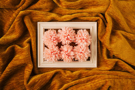 Creative concept of white wood frame with pink spring flowers against golden yellow fabric cloth wave background. Minimal design with copy space.の写真素材