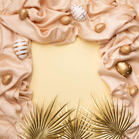 Minimal concept palm leaves with a golden easter eggs on a silk or satin fabric against pastel background with copy space.の写真素材