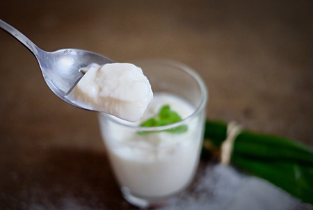 Coconut pudding in the spoon with grass cup on wood table.