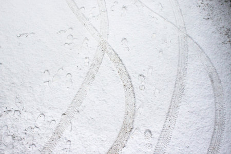 Cars tire tracks and human footprint on a thin layer of fresh snow. Top views.
