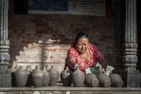 BHAKTAPUR, NEPAL? AUGUST 13, 2018: Nepalese woman making pottery in Pottery square, a public square full of pottery wheels and rows of clay pots which are made by old fashioned way drying in the sunのeditorial素材