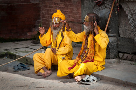 KATHMANDU, NEPAL - AUGUST 14, 2018: Unidentified Hinduist Sadhu with traditional yellow painted faces sitting at Durbar Square, Kathmandu - Nepalのeditorial素材
