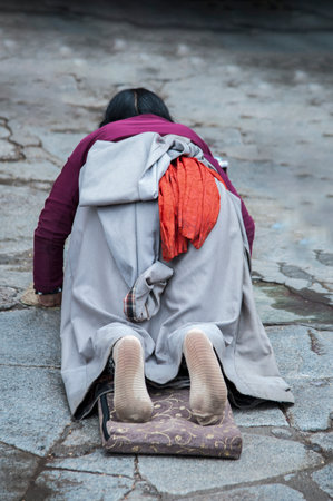 LHASA, TIBET, CHINA - AUGUST, 17 2018: Female pilgrim lying on the floor after prostrating herself. Doing the "Barkhor Kora", a devotional pilgrim circuit around the exterior of the old Jokhang Templeのeditorial素材