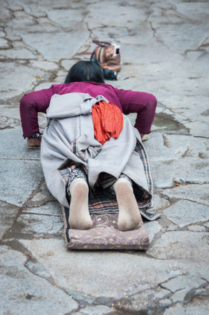LHASA, TIBET, CHINA - AUGUST, 17 2018: Female pilgrim lying on the floor after prostrating herself. Doing the "Barkhor Kora", a devotional pilgrim circuit around the exterior of the old Jokhang Templeのeditorial素材