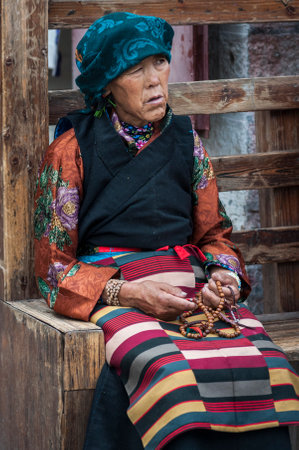 LHASA, TIBET, CHINA - AUGUST, 17 2018: Old tibetan woman in traditional clothes sit on a bench nearby Jokhang templeのeditorial素材